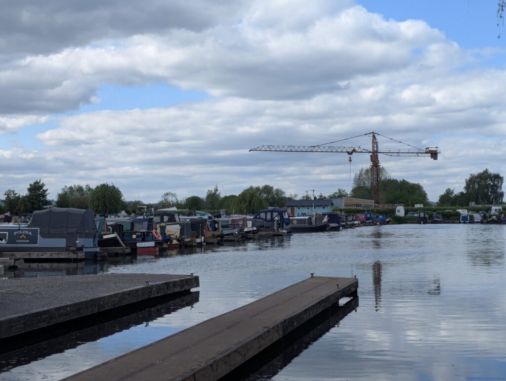 Picture of a marina filled with boats. A large crane can be seen in the background and in the water's reflection.