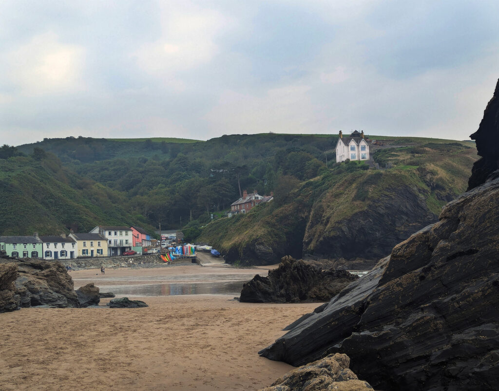 Landscape picture of a coastal town. It is surrounded by hills, with a prominent house on one of them.