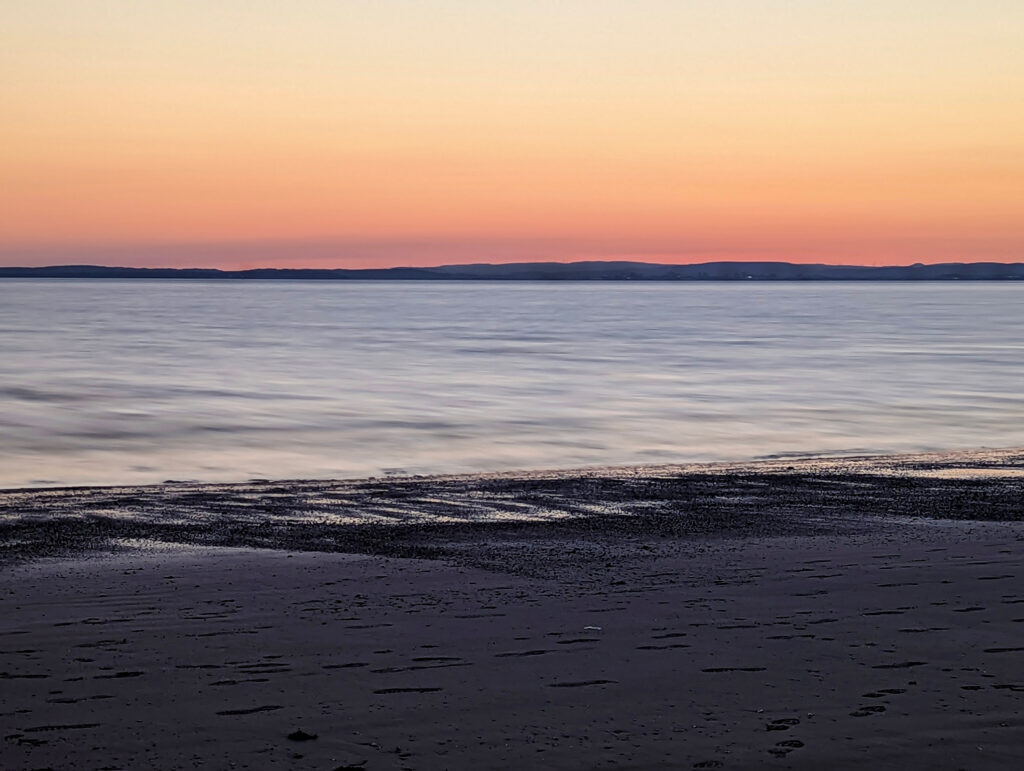 Long exposure image of a beach. The sun has set and you can faintly see a city in the background (Cardiff).
