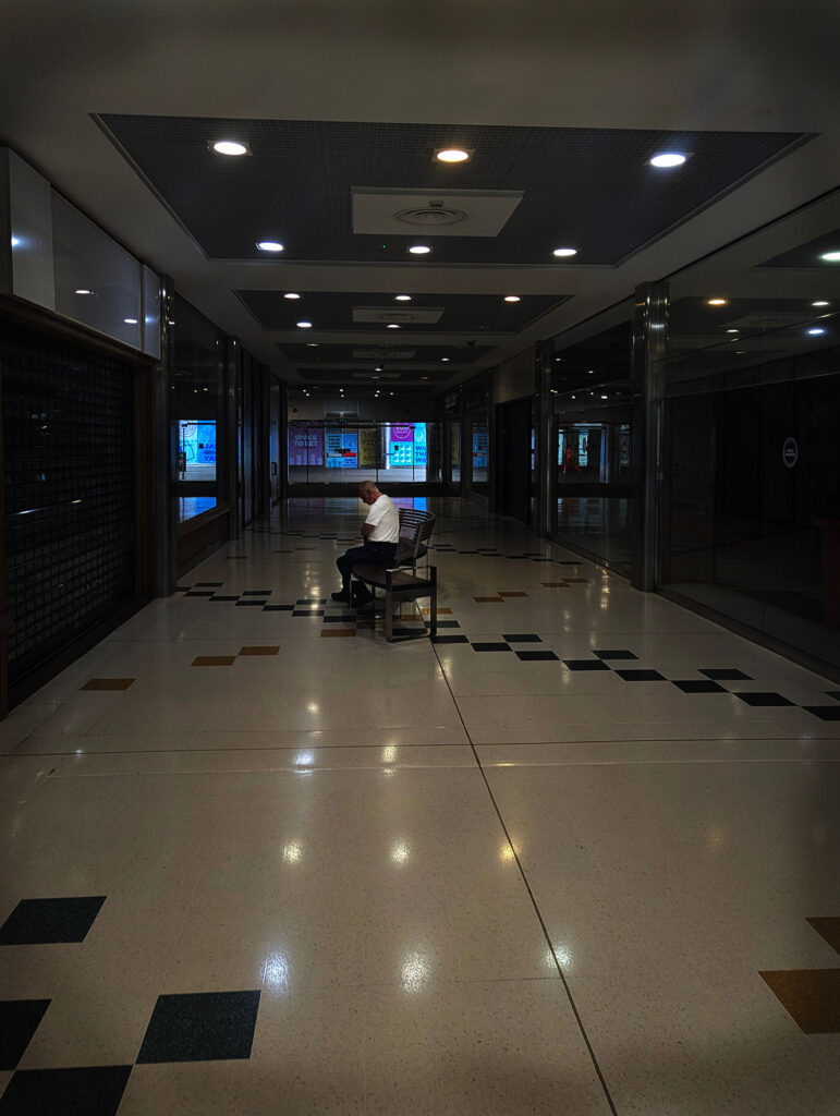 A picture of a man being sat alone in a shopping centre