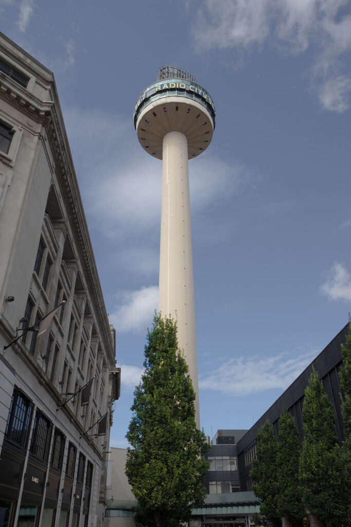 A concrete looking tower going much higher than a tree which it seems to be compared against