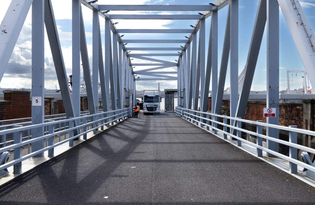 A picture of a person opening gates for a truck to leave a port area via bridge