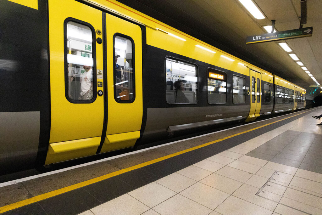 A picture of a bright yellow and black train at a train station platform, people are standing on the train getting ready to leave.